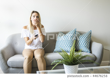 Women watching TV on the sofa at home with remote control 44676258