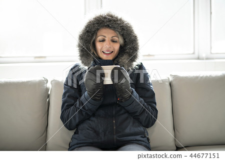Woman have cold drink coffee on the sofa at home with winter coat Woman have cold drink coffee on the sofa at home with winter coat 44677151