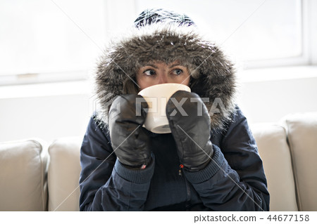 Woman have cold drink coffee on the sofa at home with winter coat 44677158