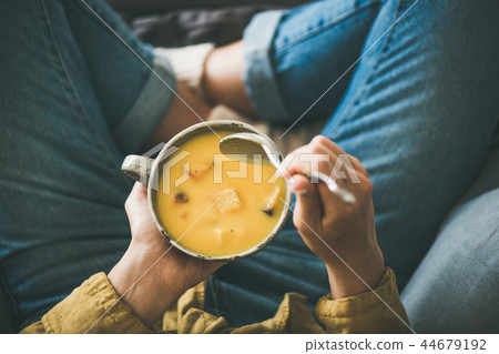 Female keeping mug of warming pumpkin yellow cream soup 44679192