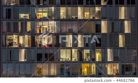Windows of the multi-storey building of glass and steel lighting inside and moving people within timelapse 44682766