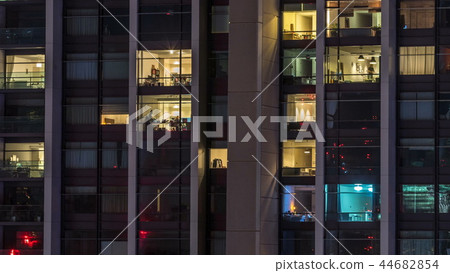 Windows of the multi-storey building of glass and steel lighting inside and moving people within timelapse 44682854