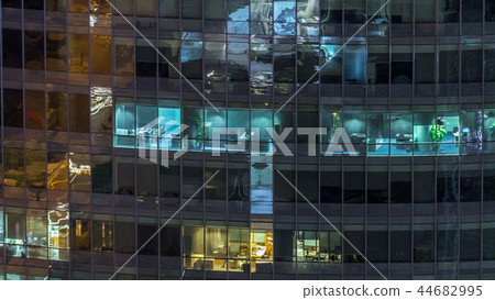 Windows of the multi-storey building of glass and steel lighting inside and moving people within timelapse 44682995