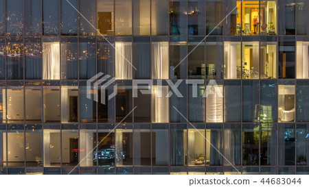 Windows of the multi-storey building of glass and steel lighting inside and moving people within timelapse 44683044