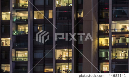 Windows of the multi-storey building of glass and steel lighting inside and moving people within timelapse 44683141