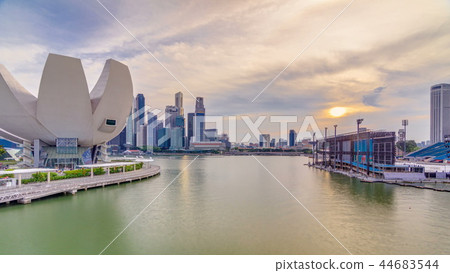 Futuristic architecture flower shape design of the Art Science museum at the foreground timelapse and skyscrapers skyline city of Singapore. Futuristic architecture flower shape design of the Art Science museum at the foreground timelapse and skyscrapers skyline city of Singapore. 44683544