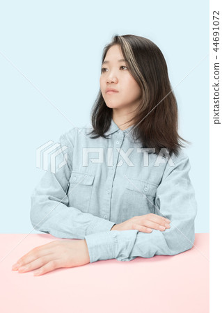 The serious business woman sitting and looking at left against blue background. The serious business woman sitting and looking at left against blue background. 44691072