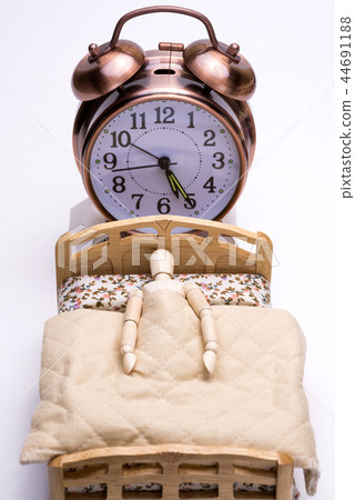 A doll sleeping on the bed and an alarm clock placed behind it A doll sleeping on the bed and an alarm clock placed behind it 44691188