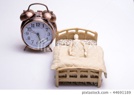 A doll sleeping with a bed and an alarm clock placed aside A doll sleeping with a bed and an alarm clock placed aside 44691189