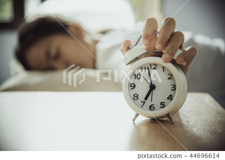 A white alarm clock rests on a table with a woman 44696614