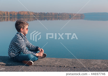 Child sitting at waterfront in warm autumn light Child sitting at waterfront in warm autumn light 44697746