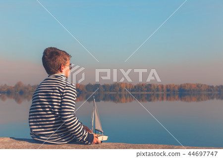 Child playing with sailing boat in beautiful light Child playing with sailing boat in beautiful light 44697747