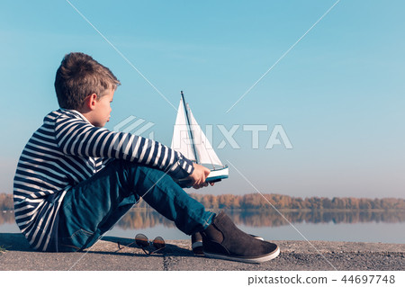 Child playing with sailing boat in beautiful light Child playing with sailing boat in beautiful light 44697748