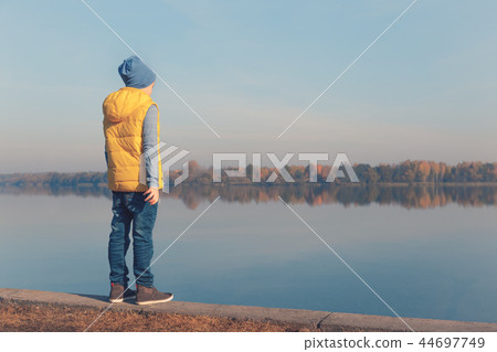 Child standing at waterfront in warm autumn light Child standing at waterfront in warm autumn light 44697749