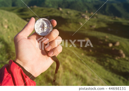 Man searching direction with a compass in hand in the summer mountains. View point on the background Man searching direction with a compass in hand in the summer mountains. View point on the background 44698131