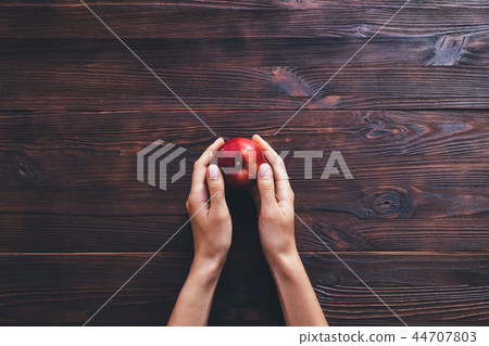 Woman's hands holding one apple on dark background Woman's hands holding one apple on dark background 44707803