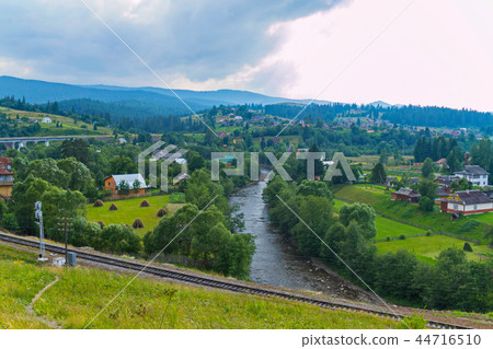 village on a green plain with a railway and a moun village on a green plain with a railway and a moun 44716510