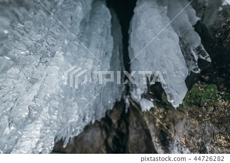 Winter Baikal. Olkhon Island. Ice grotto. Thick blue ice and icicles on the coastal rocks of Olkhon 44726282
