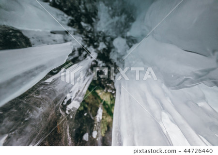 Winter Baikal. Olkhon Island. Ice grotto. Thick blue ice and icicles on the coastal rocks of Olkhon 44726440