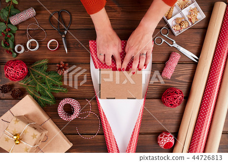 Woman s hands wrapping Christmas gift on dark wooden background. 44726813