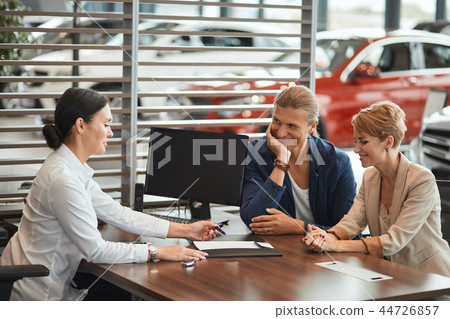 Beautiful young couple signs documents at dealership showroom. Beautiful young couple signs documents at dealership showroom. 44726857