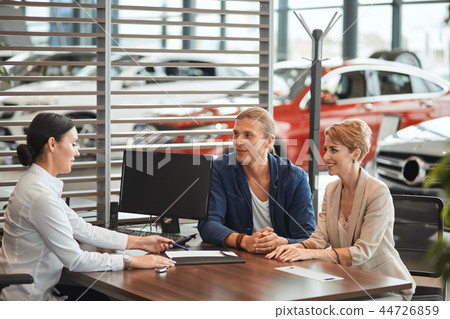 Beautiful young couple signs documents at dealership showroom. Beautiful young couple signs documents at dealership showroom. 44726859