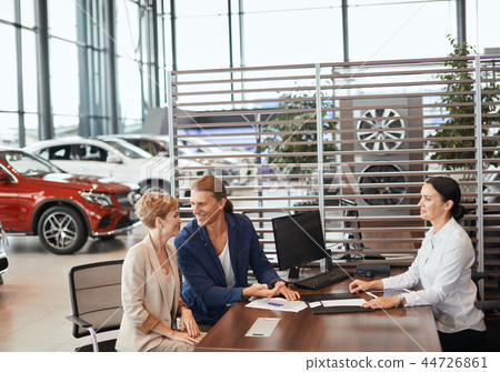 Beautiful young couple signs documents at car dealership office. Beautiful young couple signs documents at car dealership office. 44726861