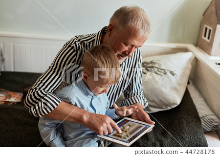 Grandfather and grandson using digital tablet while sitting on couch 44728178