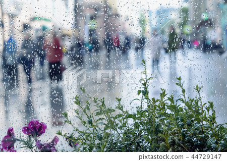 Raindrops on window glass, blurred unrecognizable people walk on road in rainy day. View from the Raindrops on window glass, blurred unrecognizable people walk on road in rainy day. View from the 44729147