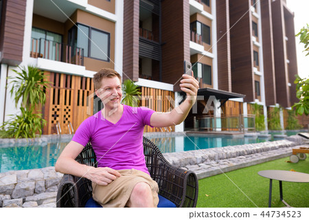 Man sitting outdoors and taking selfie with mobile phone 44734523