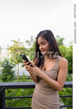 Beautiful Asian woman texting using mobile phone outdoors Beautiful Asian woman texting using mobile phone outdoors 44734545