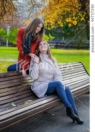 Two girlfriends sitting side by side on bench Two girlfriends sitting side by side on bench 44737290
