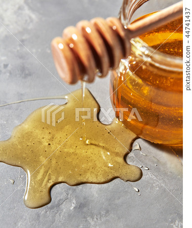 A puddle of a natural floral sweet dessert and dripping honey from wooden honey dipper on a gray A puddle of a natural floral sweet dessert and dripping honey from wooden honey dipper on a gray 44741437