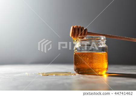 Wooden honey spoon above on a glass jar full natural organic syrup in a glass pot on a gray stone 44741462