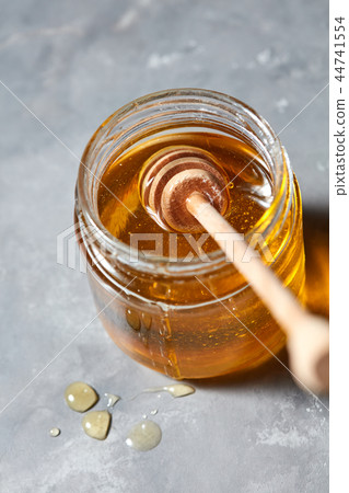 Wooden stick in a glass jar with fresh natural organic honey on a gray concrete table. Jewish New 44741554