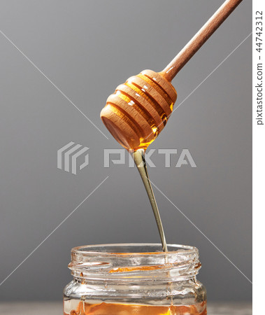 Dripping meadow organic natural honey from wooden dipper into a pot on a gray backgroun, pure raw 44742312