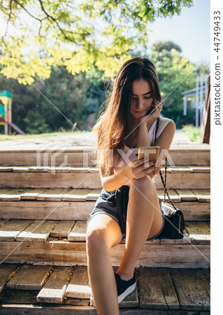 Girl sitting on wooden bench outside Girl sitting on wooden bench outside 44749433