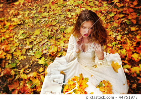 Autumn fashion dress woman sitting fall leaves city park outdoor. 44751975