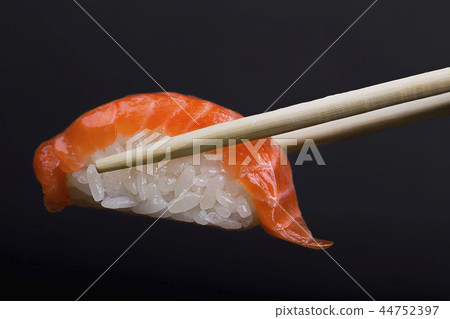Chopsticks holding salmon sushi on black backgroun 44752397