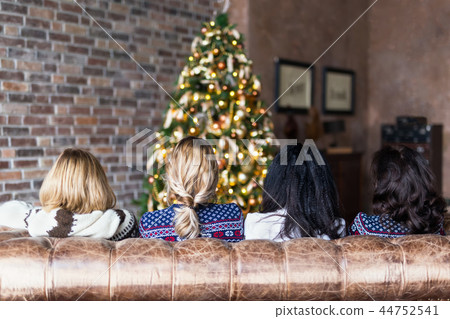 Young women sitting on the sofa near Christmas tree in cozy loft Young women sitting on the sofa near Christmas tree in cozy loft 44752541