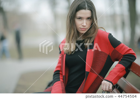 girl is sitting on a garden bench / beautiful model posing sitting in coat on bench in city park, beautiful girl 44754504