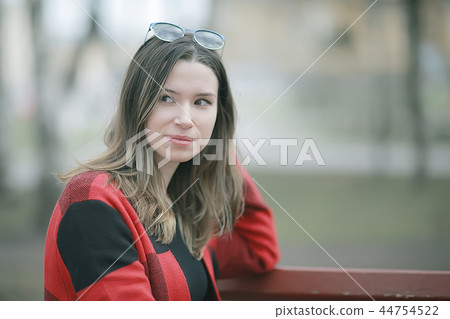 girl is sitting on a garden bench / beautiful model posing sitting in coat on bench in city park, beautiful girl 44754522