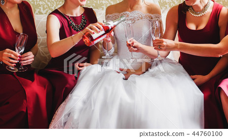 bride and her friends in red dresses at wedding pour champagne on glasses 44760100