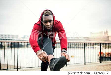 A young sporty black man runner tying shoelaces outside in a city. 44768037