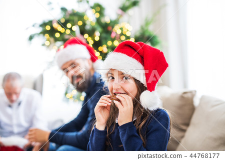A small girl with Santa hat and her father and grandfather sitting on a sofa at Christmas time. A small girl with Santa hat and her father and grandfather sitting on a sofa at Christmas time. 44768177