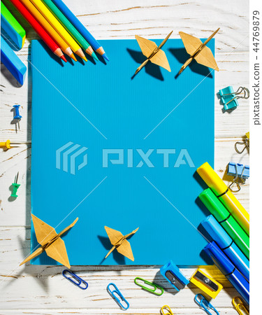In the center there is a blue notebook, pencils around it, markers. In the center there is a blue notebook, pencils around it, markers. 44769879