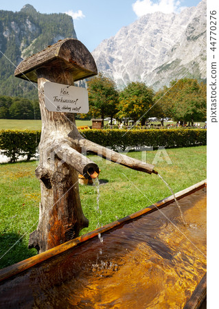 wooden water supply and Alps with fresh green meadows and blooming flowers and snowcapped mountain wooden water supply and Alps with fresh green meadows and blooming flowers and snowcapped mountain 44770276