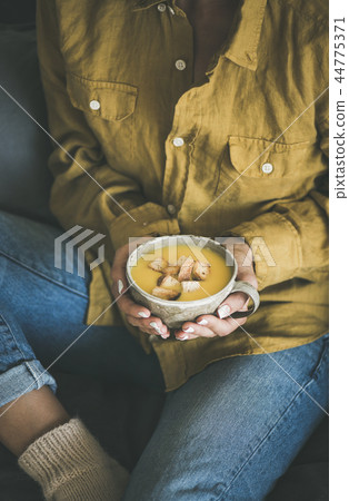 Woman sitting and holding warming pumpkin soup in mug 44775371
