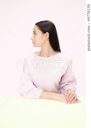 Serious business woman sitting at a table on a pink background Serious business woman sitting at a table on a pink background 44776156