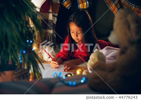 Merry Christmas and Happy Holidays. Cute little child girl writes the letter to Santa Claus near 44776243